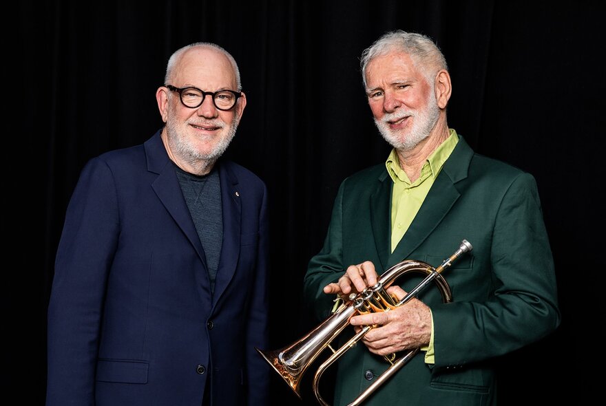 Musicians Paul Grabowsky and Vince Jones (holding a trumpet) smile against a black backdrop.