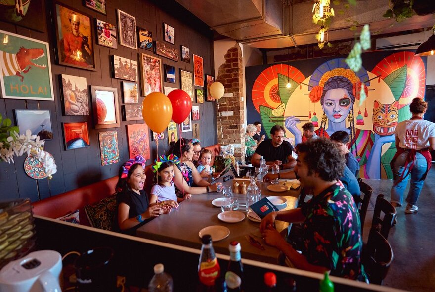 A family party happening at a Latin/Asian fusion restaurant with a colourful mural and balloons.