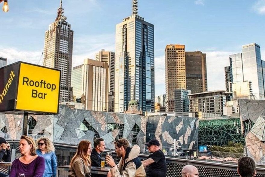 Daytime view of Transit Rooftop Bar with a few patrons and the Melbourne skyline. 