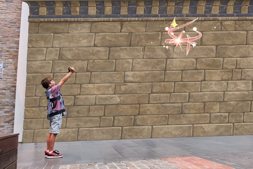 A child engaging in an immersive augmented reality adventure game standing in front of a brick wall and holding a digital device up high. 
