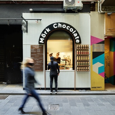 External of Mork Chocolate window, with customer and server at window, and blurred pedestrian walking past.