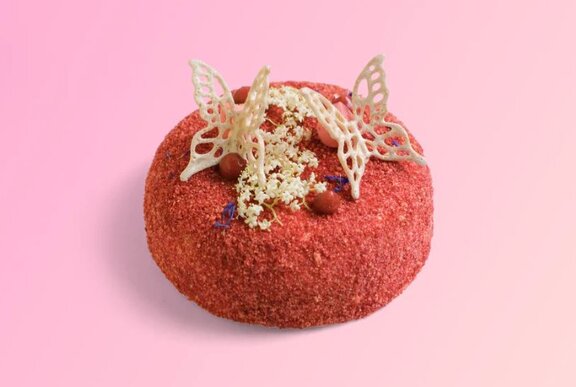 A small, round red cake decorated with white chocolate butterflies and small white and red edible embellishments.