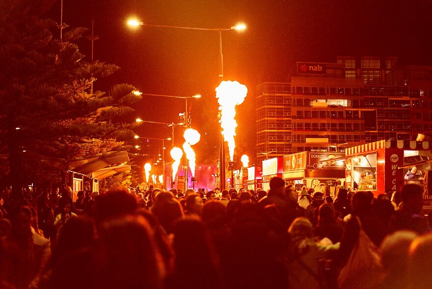 An orange glow illuminating a crowd at the Firelight Festival and fire torches shooting into the air. 
