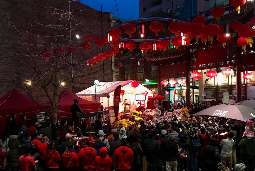Outdoors at night at a Chinese festival with red lanterns and a large crowd