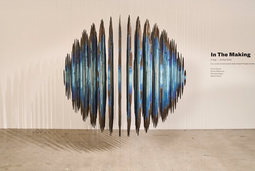 A spherical shaped sculpture appearing to hover in front of a white wall; an installation view of the exhibition In the Making at Craft Victoria's gallery space.
