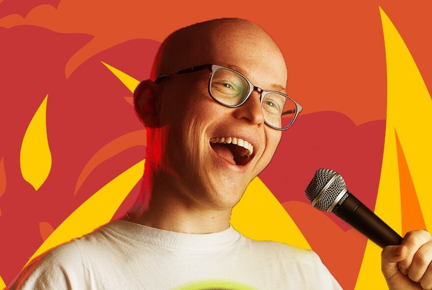 Comedian Danny Sewell, a young smiling man wearing glasses and holding a microphone against a yellow and red backdrop.