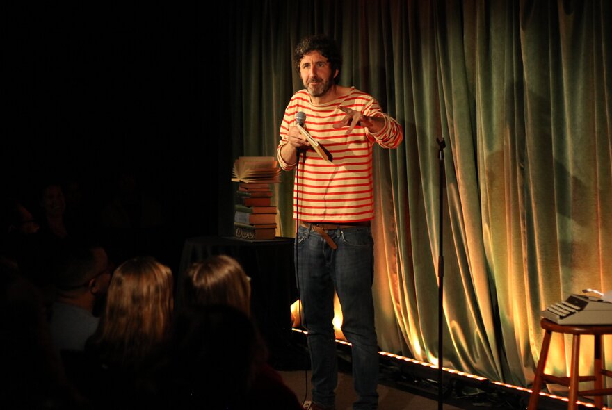 A stand up comedian on a small stage performing in front of an audience.