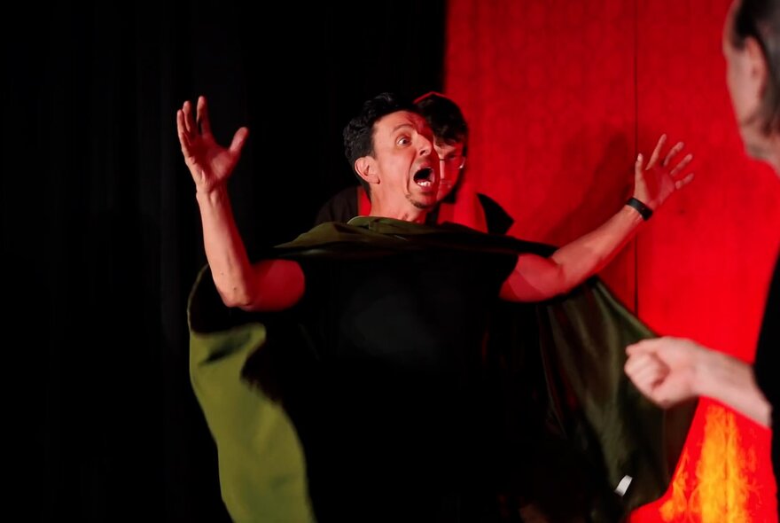 An actor on stage looking amazed, their arms outstretched, performing as part of an impro theatre ensemble.