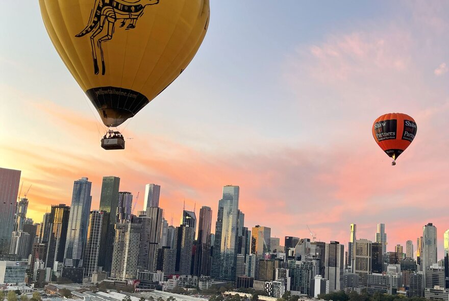 Two hot air balloons floating above Melbourne at dawn.