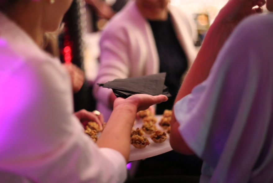 People selecting food from a waiter holding a tray.