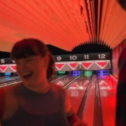 Laughing person in front of bowling alley lanes lit by red light.