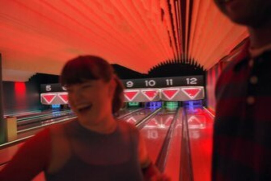 Laughing person in front of bowling alley lanes lit by red light.