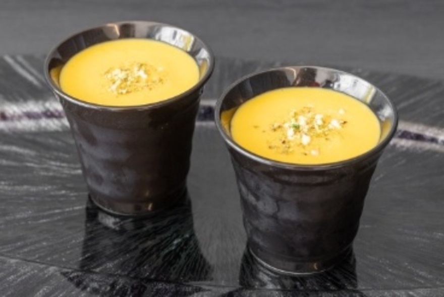 Two small black cup-like dishes of yellow dessert with nuts sprinkled on top.