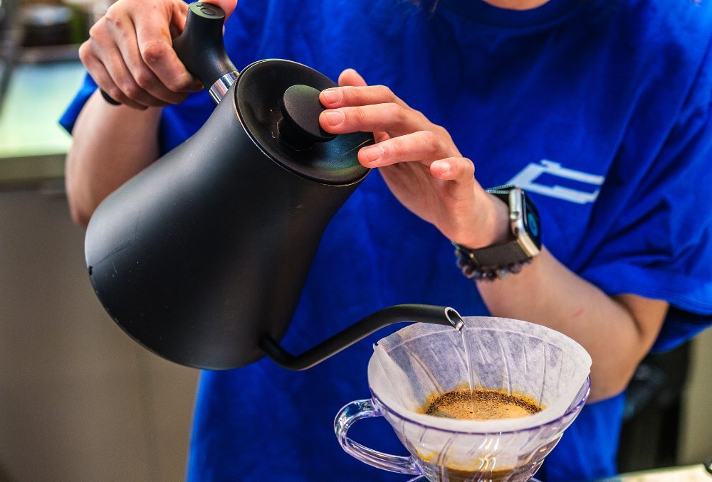 A barista pouring water through a coffee filter. 