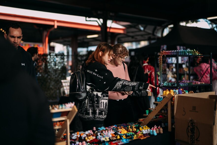 Stalls at the Queen Vic Market selling collectables, with people walking around, browsing and pointing at items on display.