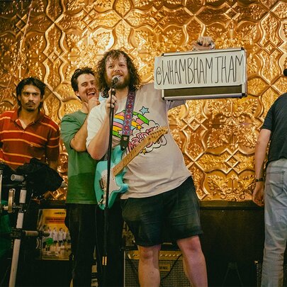 The four members of the comedic Wham Bam Thank You Jam Band on a stage in front of a pressed metal wall.