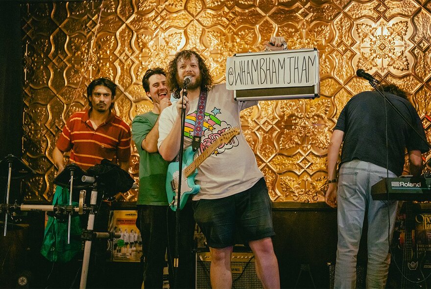 The four members of the comedic Wham Bam Thank You Jam Band on a stage in front of a pressed metal wall.