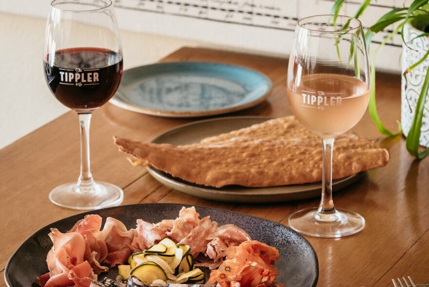 A table with antipasto and bread and two glasses of wine. 