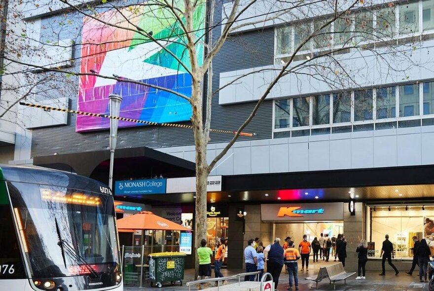 Exterior of Kmart Centre on Bourke Street showing front of building, pedestrians milling around the entrance and a tram.