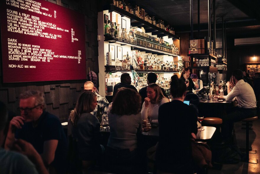 Patrons seated at tables and around the bar counter at a small cosy bar.