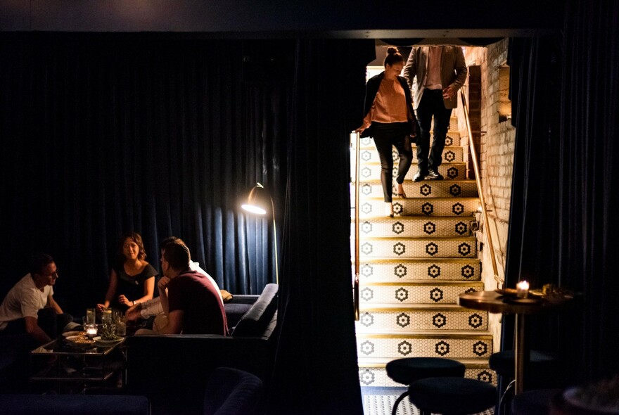 People coming down the stairs into a dimly-lit bar.