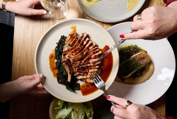 Someone passing a plate of meat over a table of Italian dishes.
