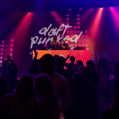 An audience watching two DJs perform a Daft Punk tribute show in a dark nightclub.