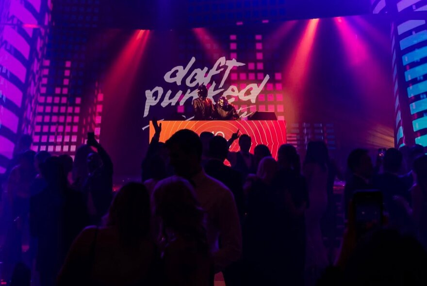 An audience watching two DJs perform a Daft Punk tribute show in a dark nightclub.