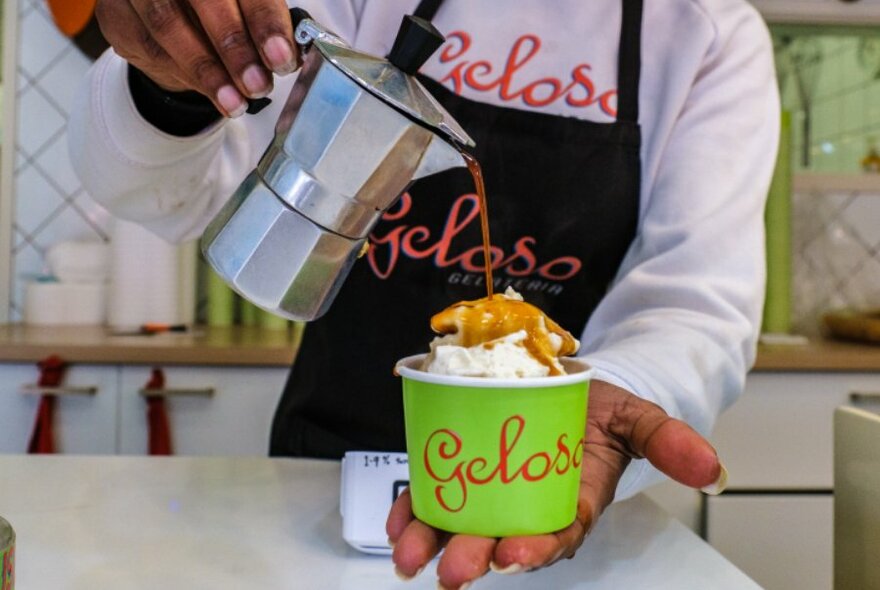 Someone pouring a pot of coffee over a cup of ice cream.