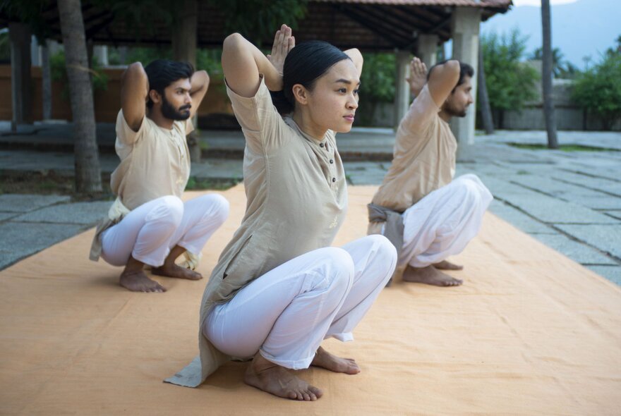 Three people outdoors in seated yoga poses, with their hands behind their heads.