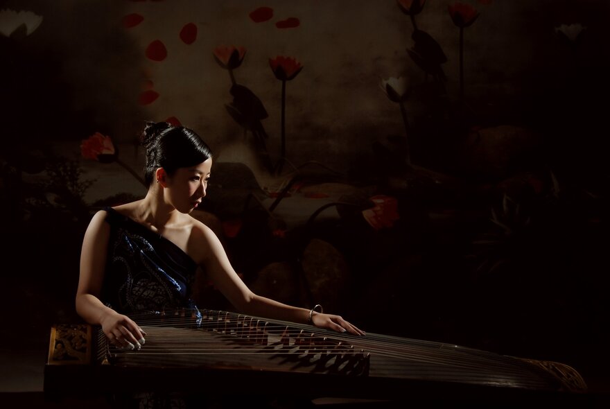Portrait of musician, Mindy Meng Wang, glamorously dressed in an evening gown, alongside her instrument, the Chinese guzheng.