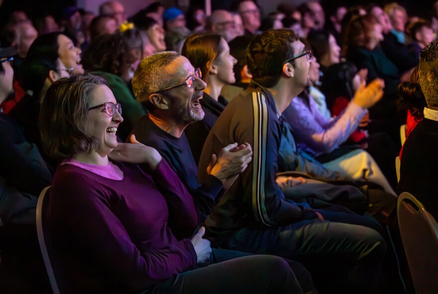 Audience members seated in rows, clapping and laughing.