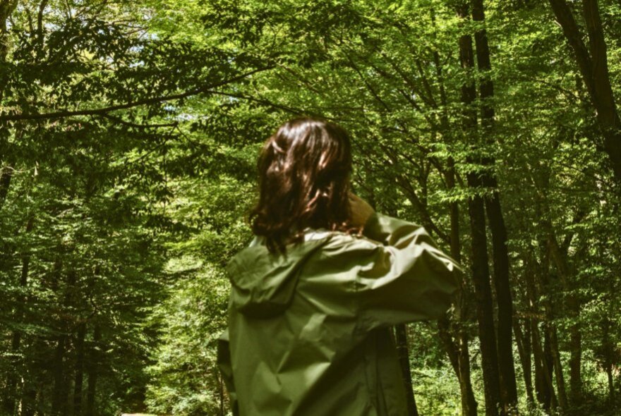 Person wearing a green coat, standing camouflaged in a forest.