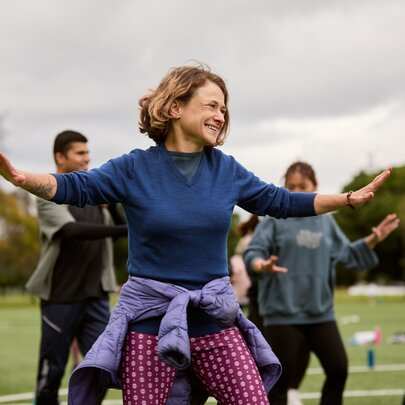 A group of people participating in an outdoor group fitness or yoga class on a grassy field under an overcast sky.