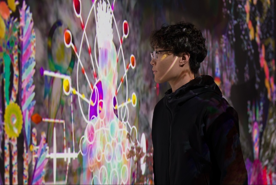 A person in a gallery setting, staring intently at a  colourful projection on a wall.