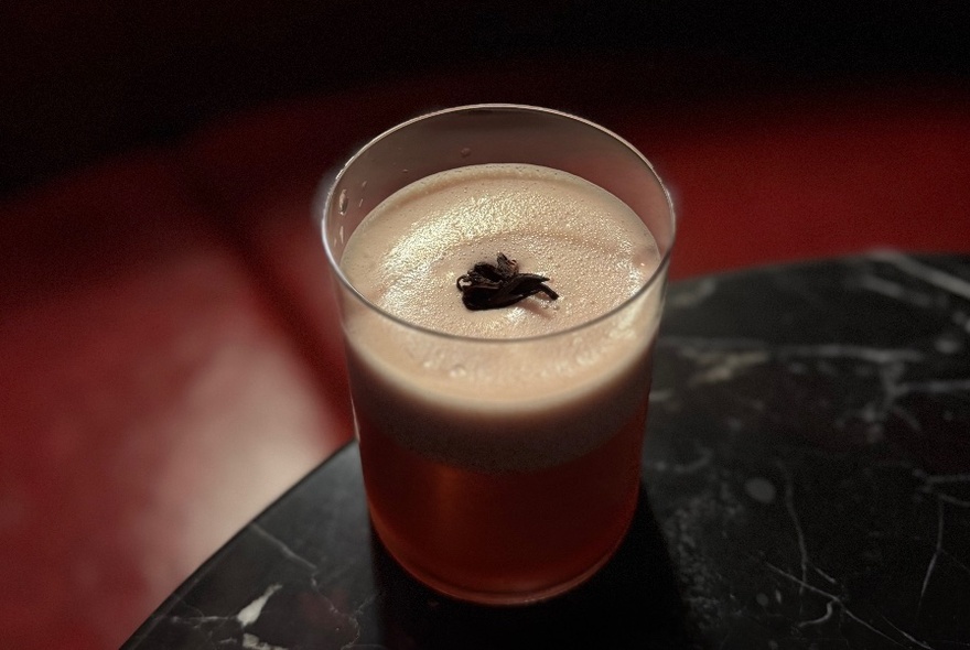 A cocktail in a short ball tumbler, on the edge of a round marble table.