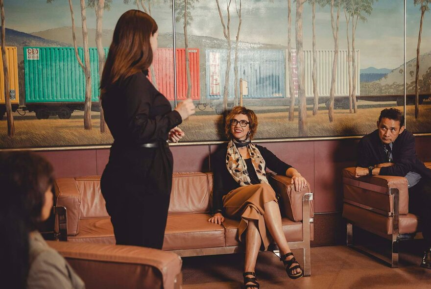 Four people on a tour of Arts Centre Melbourne, seated in a foyer, with a large mural behind them.
