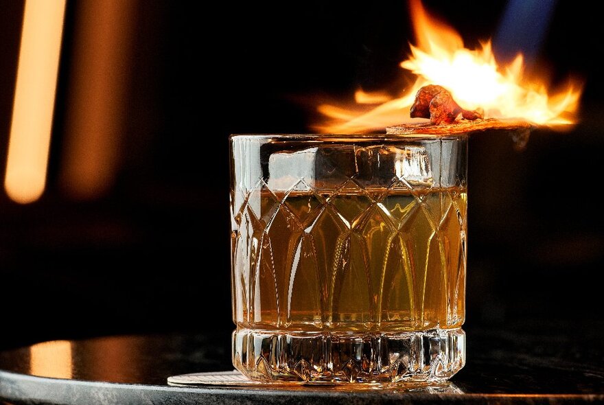 A cocktail in a short glass with a flaming garnish.