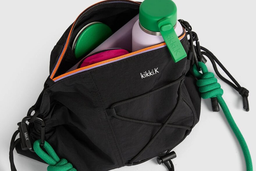 A black bag with a green strap with a water bottle and note book inside