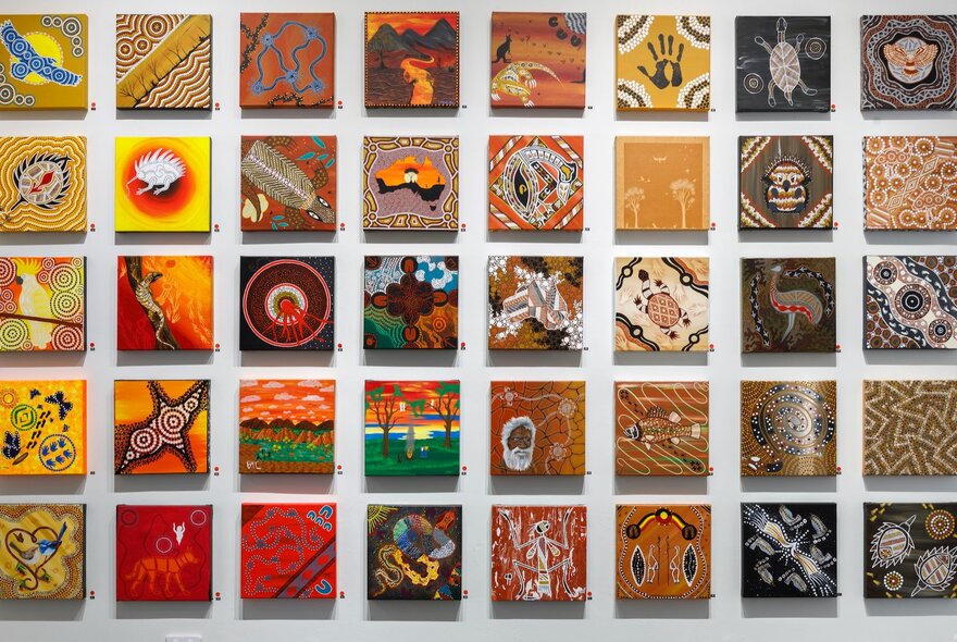 An installation view of many paintings of the same size (30x30cm) displayed on a wall in a gallery. 