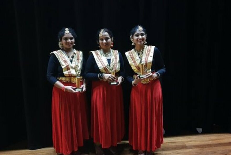 Three traditionally dressed Indian women wearing gold tops and red skirts.