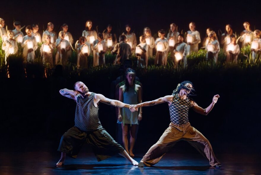 Three dancers on a stage, behind them on an raised platform is a standing choir.