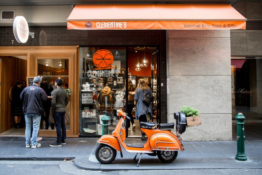 Orange motor scooter parked outside Clementines store, matching the colour of the shop logo.