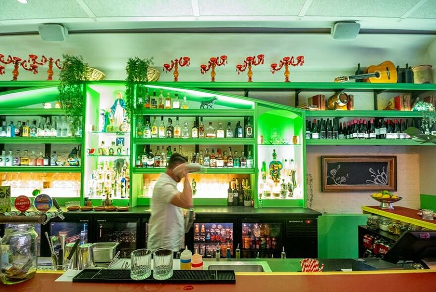 Person carrying something in a bright green bar area of a restaurant.