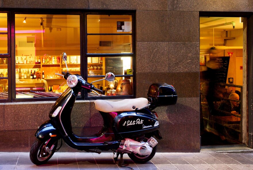 A black Vespa parked outside Il Solito Posto, a warm glow from the restaurant. 