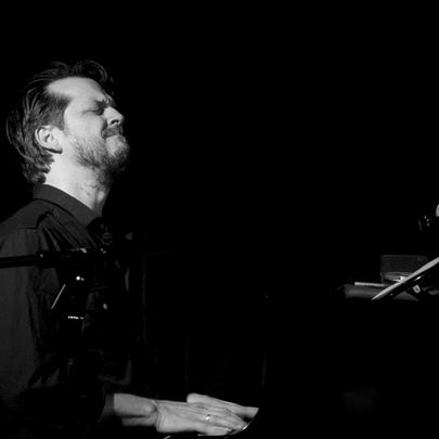 Black and white image of musician Barney  McAll seated and playing the piano, his head is tilted slightly back and his eyes are closed.