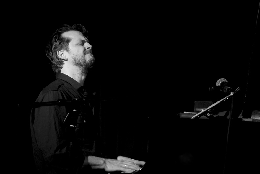 Black and white image of musician Barney  McAll seated and playing the piano, his head is tilted slightly back and his eyes are closed.