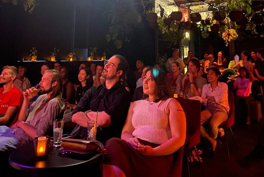 Audience seated at tables with candles in a darkened venue.