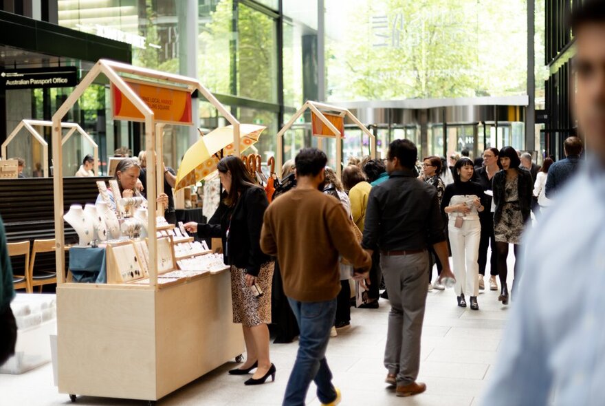 Shoppers and pedestrians walking around an indoor fashion and artisan market looking at stalls.