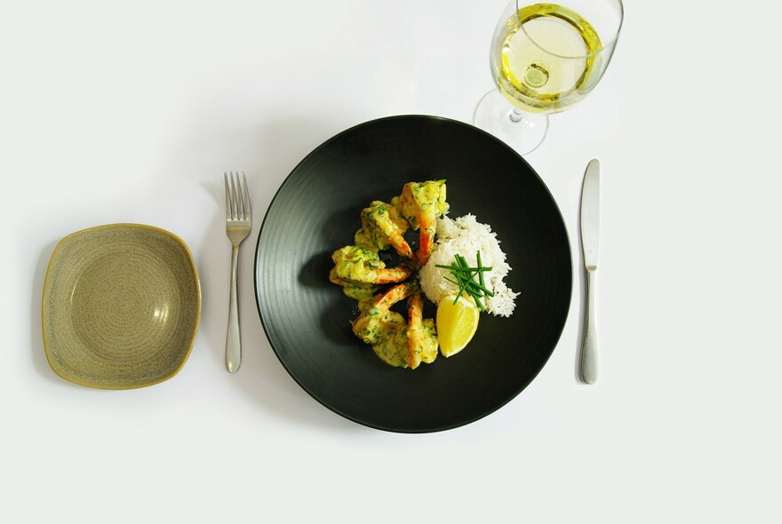 Prawns and rice in a black bowl, next to glass of white wine.